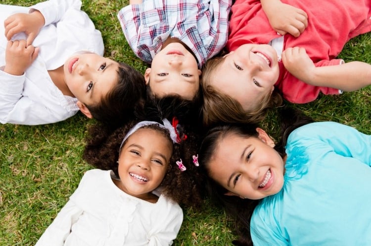 Young children lying down on the grass in a circle and are smiling