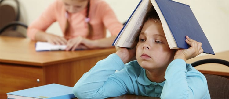 Child sitting at desk with a book open on their head