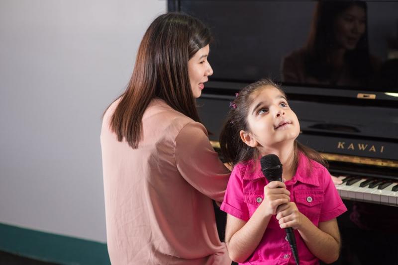 Simra sitting next to her piano accompaniest singing