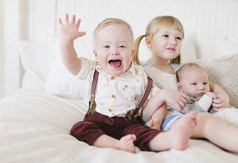 professional photo of welles and his two siblings sitting together and smiling. Welles has a big grin and waves to the camera