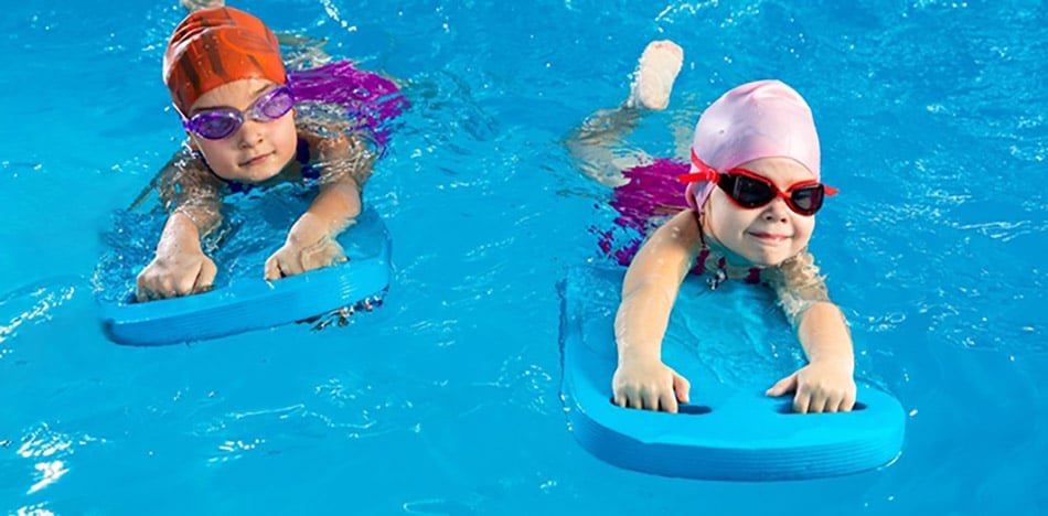 2 young children with goggle and swim caps, swimming holding paddling boards